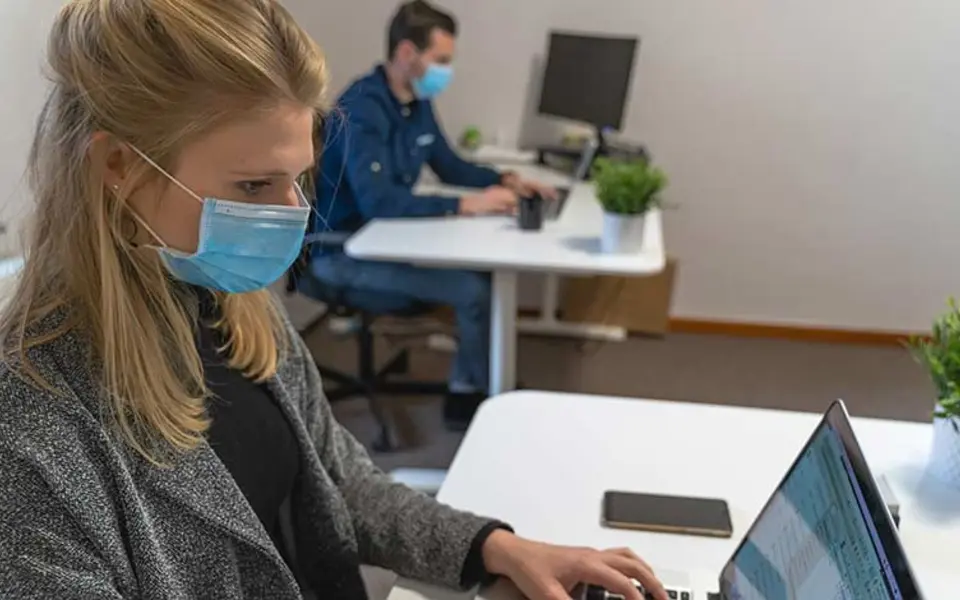 Büromitarbeiter mit Mundschutz an Schreibtischen