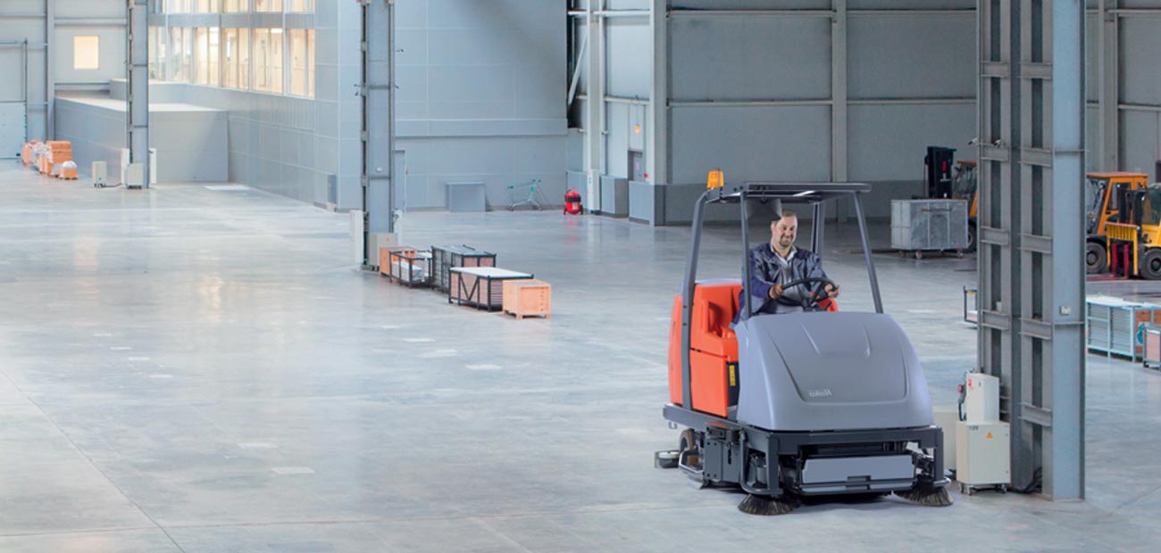 Gebäudereiniger reinigt Industriehalle mit Aufsitzkehrmaschine