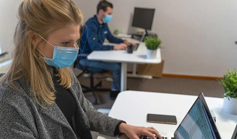 Büromitarbeiter mit Mundschutz an Schreibtischen